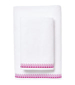 Two white hand and bath towels from the Averylily Wind and Wave Bath Collection, made with Aegean cotton, feature a pink zigzag border. One is folded atop the other against a white background. OEKO-TEX Certified for safety and comfort.