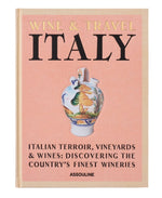 The book cover titled "Wine & Travel Italy" from Assouline showcases an illustrated vase adorned with a scenic design. The subtext, "Italian Terroir, Vineyards & Wines: Discovering the Country's Finest Wineries" by Enrico Bernardo, pays homage to Italian vineyards and wine tourism experiences.