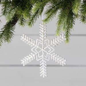 The Park Hill Collection’s Pearl Beaded Snowflake Ornament sparkles on a green pine branch, framed by iridescent glass icicles against a light gray wooden background.