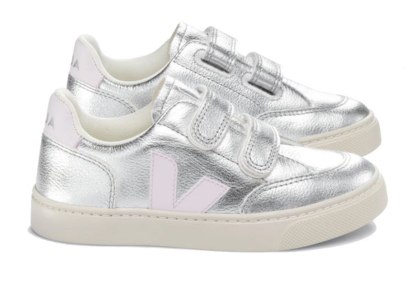 Pair of Veja Junior V-12 Velcro Sneakers with white soles and velcro straps, featuring a pink "v" logo on the side, made with organic cotton.