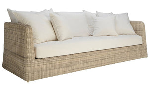 The Zeya Outdoor 3 Seater Sofa by Janus et Cie features a weather-resistant wicker frame, beige cushions, and five white throw pillows, shown against a white background.