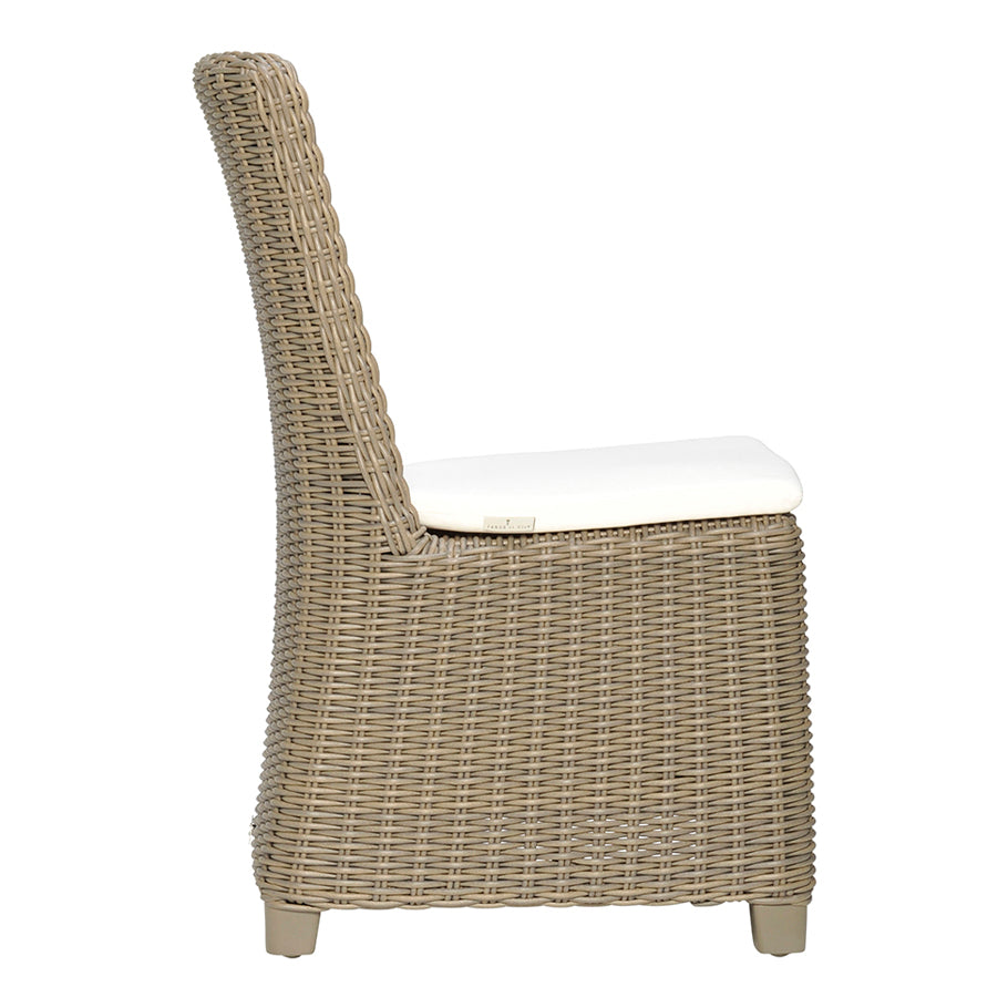 The Zeya Outdoor Dining Side Chair by Janus et Cie features weather-resistant wicker, a high back, and a white seat cushion—perfect for outdoor dining—shown in side view against a plain white background.