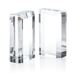 The Claire Crystal Glass Bookend Set by Zodax features two clear rectangular glass blocks with sharp edges and clean lines, serving as elegant minimalist bookends and a sophisticated addition to any bookshelf decor.