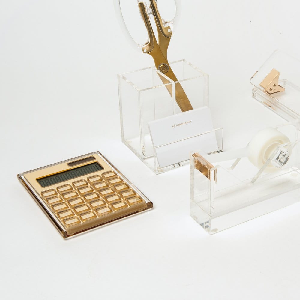 The Russell & Hazel Acrylic Gold Calculator is arranged on a white surface with an acrylic tape dispenser, gold-accented scissors holder with gold scissors, and a business card holder.