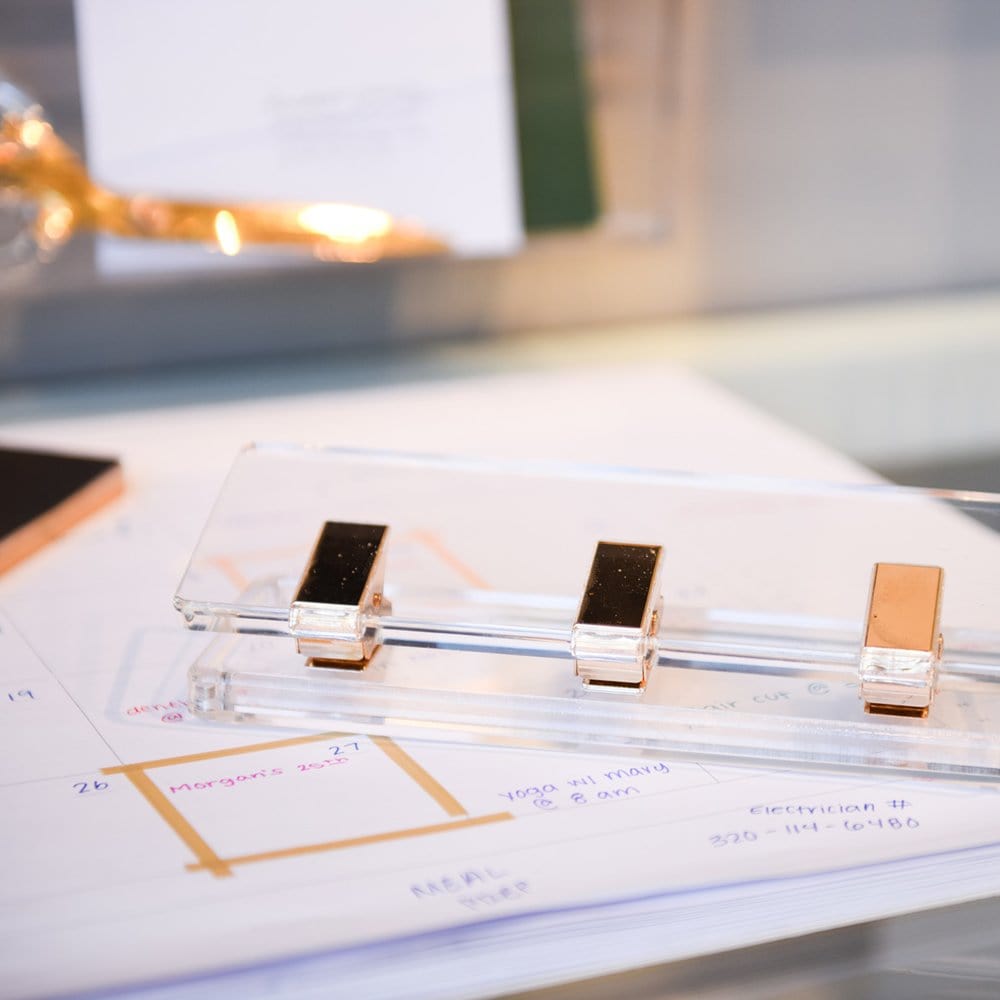 Close-up of Russell & Hazel's Acrylic Signature Hole Punch with three gold-toned clips on a desk, elegantly holding handwritten notes and adding a personal touch to the setup.
