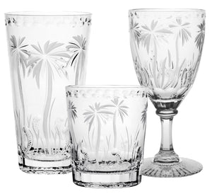 The Alexis Collection by William Yeoward Crystal features handmade crystal glasses—a tall tumbler, short tumbler, and wine glass—with hand-cut palm tree designs.
