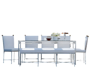 The Amalfi Dining Table in White Vermouth by Janus et Cie, paired with six white chairs and a glass tabletop, features an elegant centerpiece and sleek design—perfect for enhancing any lounge or dining space with modern style.