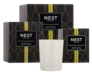 Three boxes of the Nest Amalfi Lemon & Mint Collection evoke the freshness of the Amalfi Coast, elegantly displayed behind a white glass holder Mint candle.