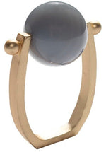 The Kim Seybert Mineral Napkin Ring features a square gold band with a large round gray semi-precious stone set between two small gold spheres—an elegant accent perfect for year-round entertaining.