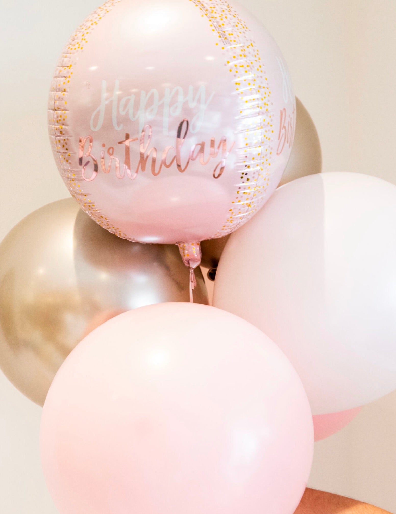 A delightful balloon bouquet featuring a bundle of Burton+Burton Solid Balloons with "Happy Birthday" text on one. The colors—pink, gold, and white—create a charming display perfect for any celebration.