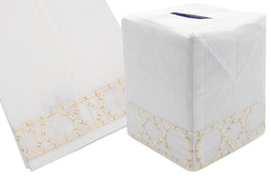 The Bamboozle Bath Collection, Cream by Haute Home, features a white Italian linen tissue box cover elegantly detailed with beige hand embroidery at the bottom edge, accompanied by a matching linen napkin with similar intricate embroidery.