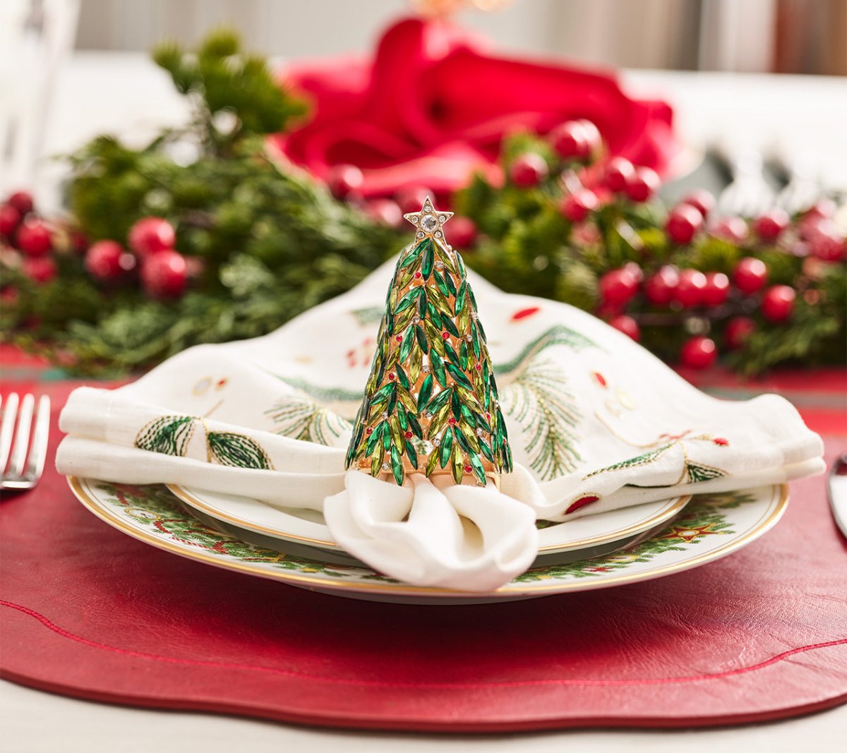 A festive table features Kim Seybert’s Christmas Tree Napkin Ring Set, holiday-inspired plates, and greenery with red berries for decoration.