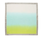 The Kim Seybert Dip Dye Napkin Set features square napkins with an ombre design, hand dipped and dyed from light cream to blue to lime green, finished with a gray trim.