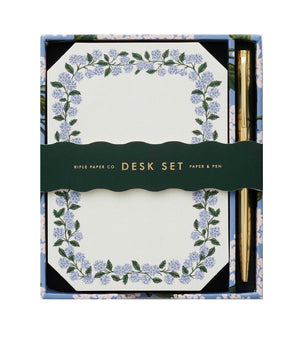 The Blue Hydrangea Desk Accessory Collection by Riffle Paper Co. includes a floral-bordered notepad and gold pen, making it the perfect addition to any workspace.