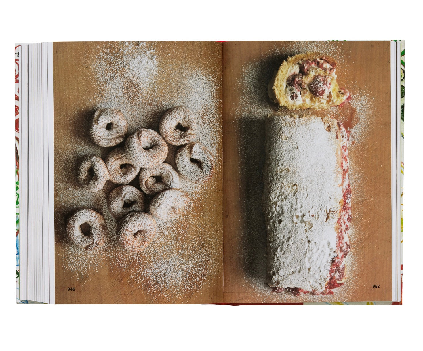 Open cookbook displaying a recipe spread with images of doughnuts and a rolled cake, sprinkled with powdered sugar from the Phaidon Spain: The Cookbook on traditional home cooking.