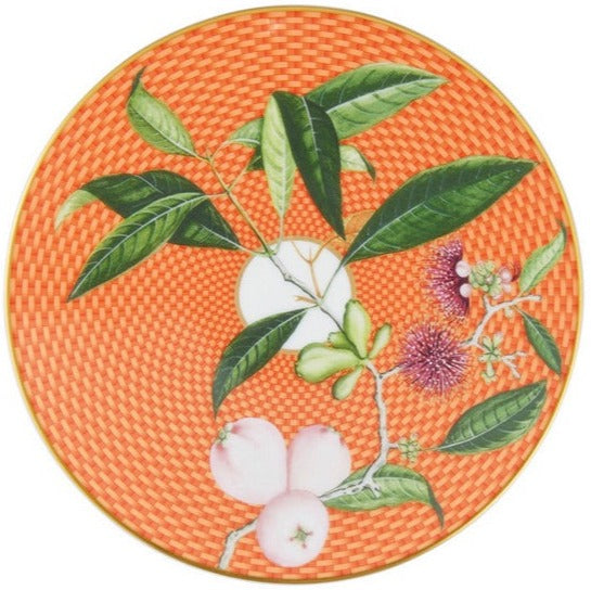 The Tresor Fleuri Orange Dinnerware Collection by Raynaud features a round orange porcelain plate with a woven texture, hand painted green leaves, pink flowers, and pale pink fruits on a branch.