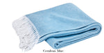 A Pezzo Throw Collection blanket by Matouk, in folded cerulean blue brushed cotton with white fringed edges, is displayed on a white background.