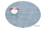 A blue Oval Placemat by Chilewich, styled with a white cup and saucer and a red fork—ideal for any dining setting. "Chambray" is seen in the lower right corner.