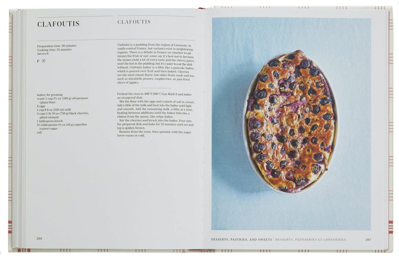 An open copy of "Classic French Recipes" by Phaidon displays a clafoutis recipe on the left page and a beautifully baked clafoutis with berries served in an oval dish on the right page, perfectly capturing the essence of authentic French home-cooking.
