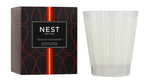 A Nest Sicilian Tangerine Candle from the Sicilian Tangerine Candle Collection sits in a clear glass holder beside its signature black and orange box, crafted with premium wax for a luxurious fragrance experience.
