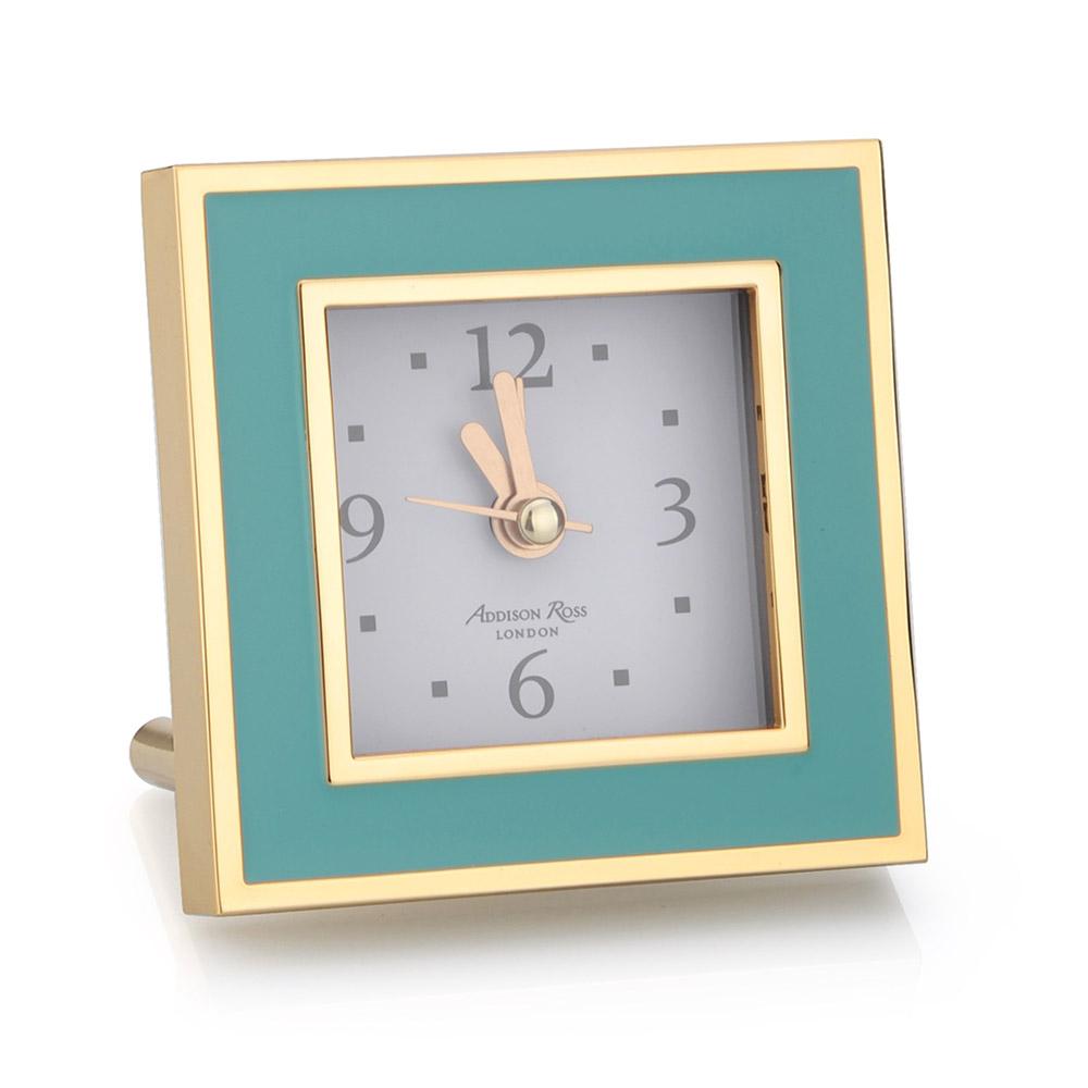 The Addison Ross Gold Square Alarm Clock Collection features a turquoise enamel frame with gold accents. It has a white dial, black numbers, and gold hands with a silent sweep movement. "Addison Ross London" is on the face, complemented by a luxury velvet back for an opulent effect.