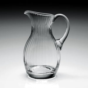 The William Yeoward Crystal Corinne Pitcher, tall and clear with vertical ridges and a curved handle, from the Corinne Collection is displayed on a gray gradient background.