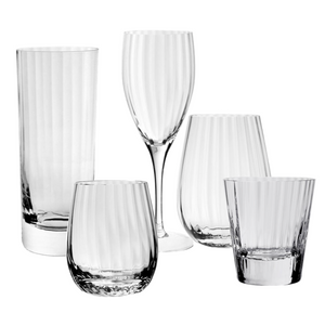 The Corinne Collection by William Yeoward Crystal includes five clear glass drinkware pieces with a vertical optic pattern: a tall glass, wine glass, and three uniquely shaped short glasses.