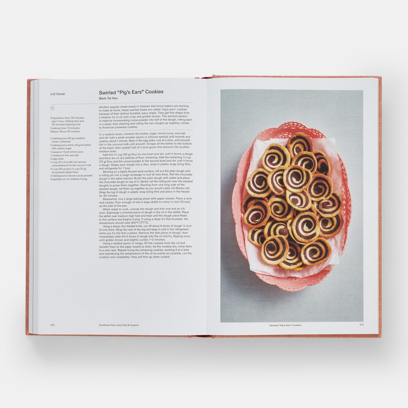 The open "Crumbs: Cookies and Sweets from Around the World" by Phaidon shows a recipe for Swirled "Pig's Ears" Cookies on the left, with a photo of them served in a pink dish on the right.
