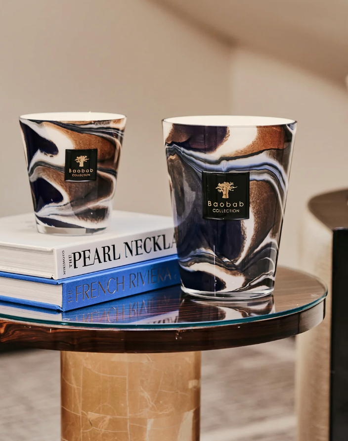 Two Baobab Collection Delta Nil Candles with a floral fragrance on a glass table with stacked books titled "Pearl Necklace French Riviera.