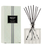 A bottle of Nest Indian Jasmine Reed Diffuser with black reeds is placed beside its patterned box, featuring notes of jasmine absolute and hints of red berries.