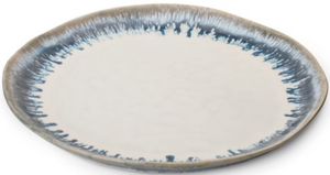 The Simon Pearce Burlington Pool Dinnerware Collection features a round ceramic plate with a beige center and a blue, irregular-patterned rim inspired by organic drip techniques.