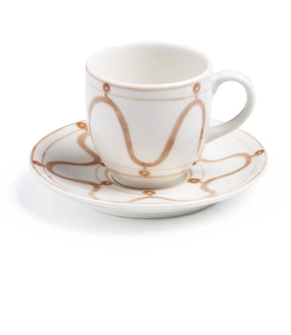 A white ceramic cup with a handle rests on a matching saucer, both from Themis Z's Serenity Beige Dinnerware Collection, featuring hand-painted brown wavy lines and circles.