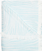 The Daasu Throw Collection by John Robshaw features a light blue and white stonewashed cotton towel with subtle wavy stripes, fringed edges, and a reversible design.