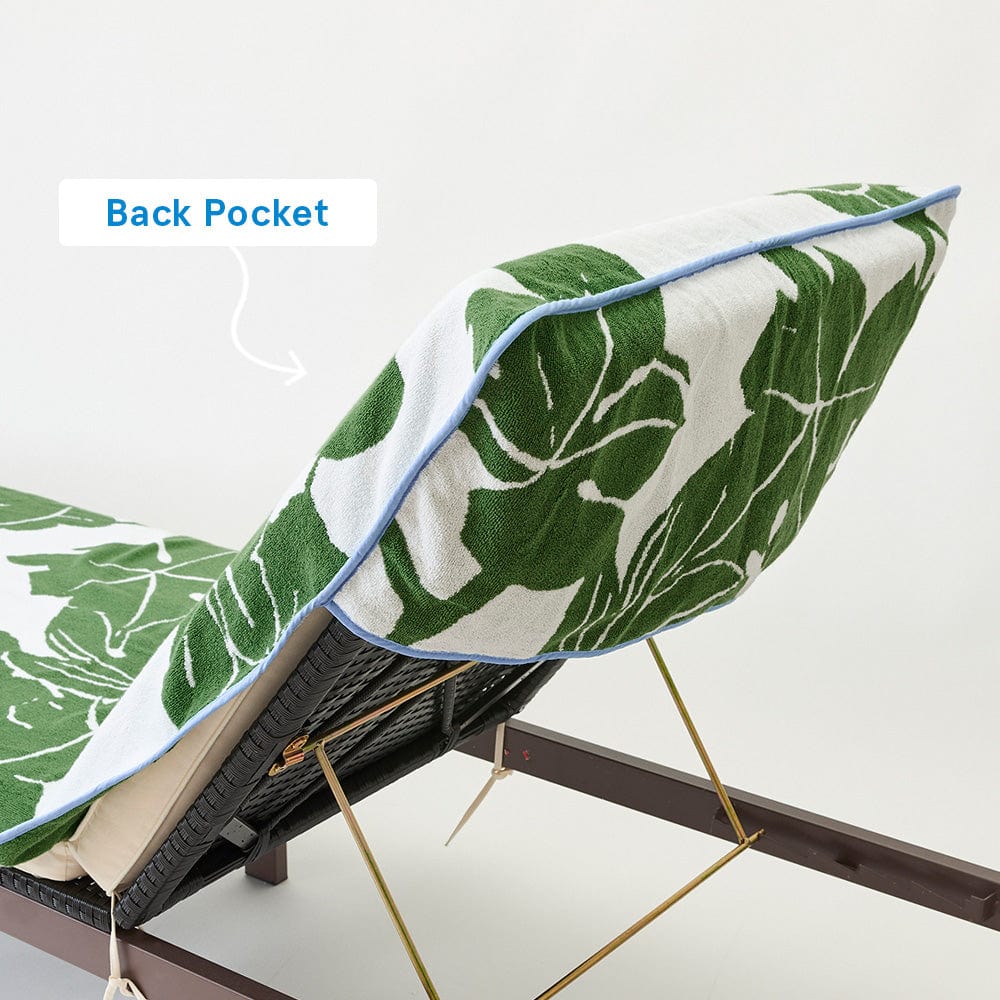 The Weezie x Peter Dunham Fig Pool Towel, from Weezie Towels, in green and white print with blue trim, drapes elegantly over a lounge chair, crafted from luxurious long-staple cotton. An arrow highlights the back pocket on the towel.