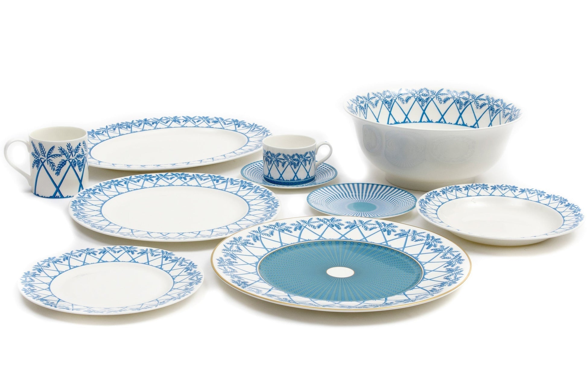 The Azure Blue Dinnerware Collection by Pink House Mustique features fine bone china plates, bowls, a mug, and a cup with saucer in blue geometric and floral patterns, elegantly arranged on a white surface.