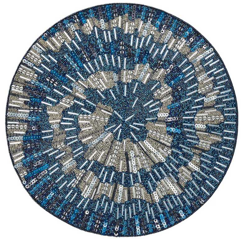 The Kim Seybert Illusion Placemat is a circular design adorned with blue, silver, and white beads and sequins in an abstract spiral pattern.