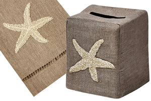 The Starfish Bath Collection by Haute Home includes a hand-embroidered tissue box cover and matching table runner in cream on flax, both featuring intricate starfish designs crafted from Italian linen.
