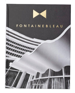 The Assouline book "Fontainebleau" features a black-and-white cover image of architectural beauty, adorned with gold lettering. It exudes luxury, reflecting the grandeur reminiscent of the iconic Fontainebleau hotel.