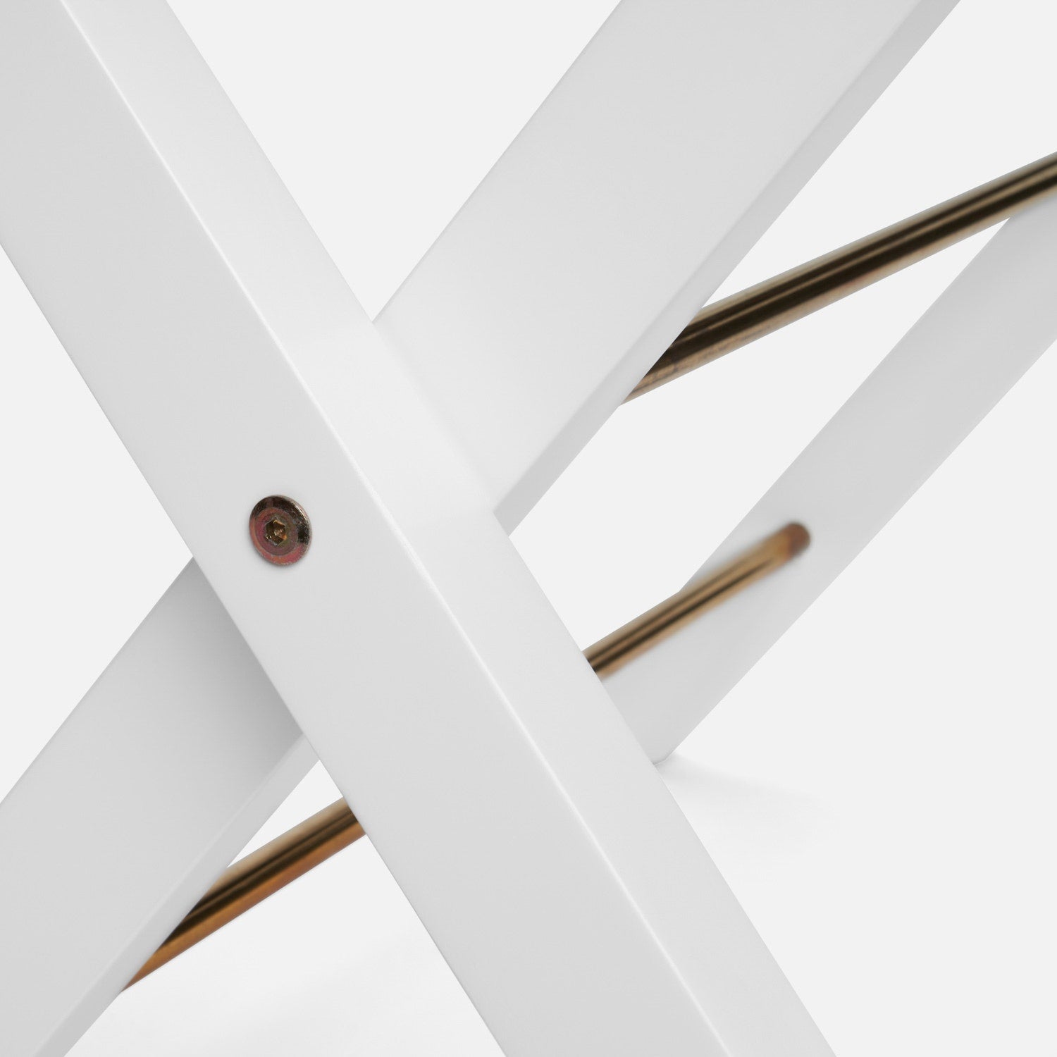 Close-up of intersecting white metal bars with a screw and two gold rods, resembling the Walvia Luggage Rack by Made Goods, featuring white duco finish and navy canvas, set against a plain surface.