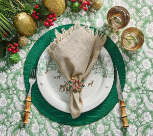 A festive holiday table is set with a deer plate, a beige napkin accented by the Kim Seybert Gem Wreath Napkin Ring Set, bamboo-handled cutlery, two glasses, and greenery with berries and gold ornaments.