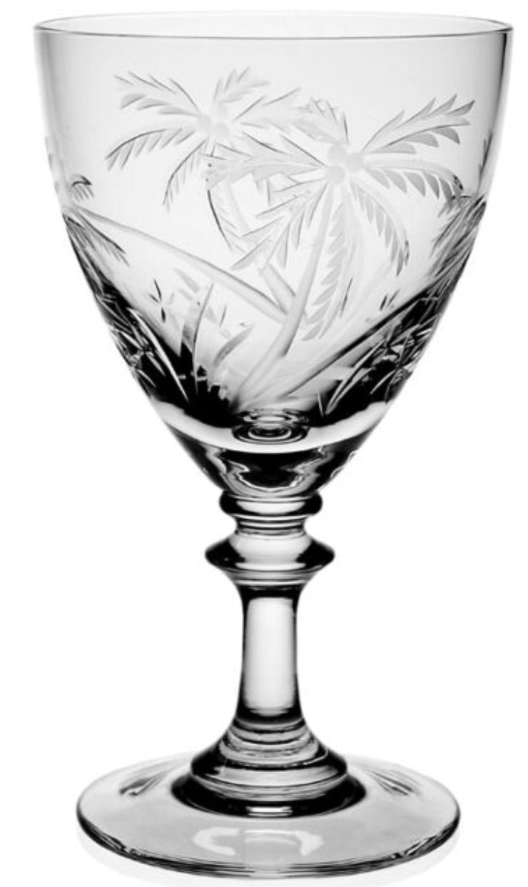 The Palmyra Drinkware Collection by William Yeoward Crystal features a clear wine glass with etched palm trees and foliage, inspired by Palmyra Atoll, set on a short stem and round base.