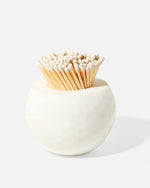 The Tart by Taylor Golf Match Striker Collection features a round white ceramic holder inspired by a golf ball, filled with wooden matches topped with white heads—an elegant accessory for match striking.