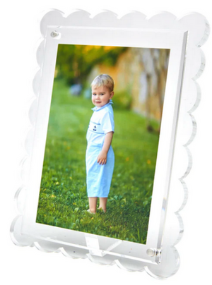 A framed photograph of a young child on green grass in a light blue outfit, with trees and a stone wall behind—displayed in our best-selling Tara Wilson Designs Scallop Frame Collection, which beautifully enhances any cherished memory.