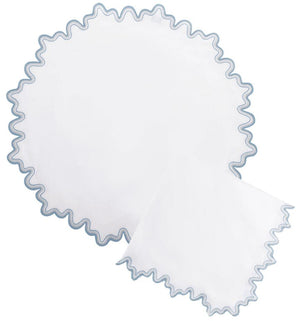 The Matouk Wave Tabletop Collection in Hazy Blue features a round white linen placemat and a matching square napkin, both accented with wavy blue embroidered edges, displayed on a white background.
