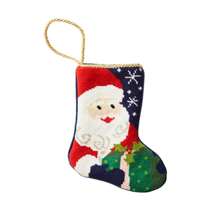 Add festive charm to your decor with the Bauble Stockings Ho Ho Ho Santa Needle Point Stocking, featuring hand-stitched Santa holding a green gift, snowflakes, and a gold hanging loop—a perfect addition to your collection.