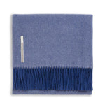 The Classic Herringbone Throw Collection by Alicia Adams Alpaca features a folded blue herringbone-patterned baby alpaca blanket with dark blue fringe, a left-side label, and is fair-trade made in Peru.