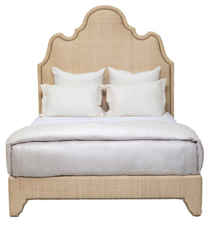 The Ingrid Bed by Oly features a tall, curved, beige upholstered headboard with nailhead detailing, and is styled with crisp white linens and four white pillows.