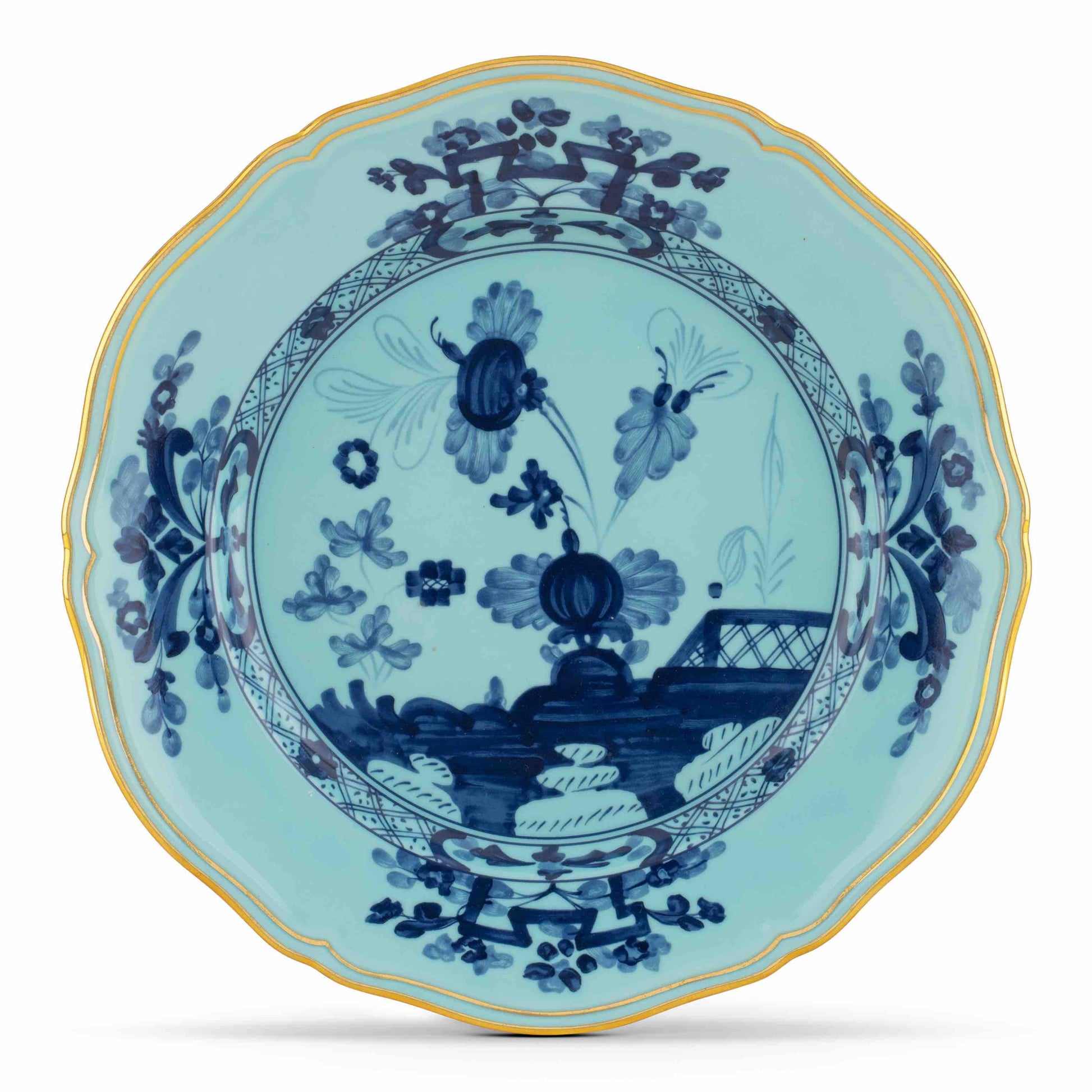Part of the Oriente Italiano Iris with Gold Dinnerware Collection by Ginori 1735, this round scalloped-edge plate showcases blue floral and landscape motifs on a light blue background accented with a slender yellow rim.