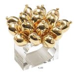 The Jubilee Napkin Ring by Kim Seybert features a clear acrylic band topped with shiny gold balloon-shaped ornaments, adding a festive accent to elegant table settings for special occasions.