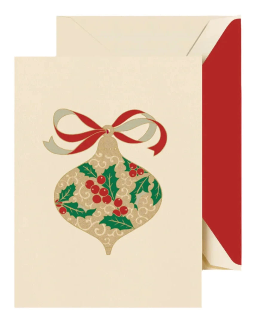 The Crane Filigree Ornament Card Set includes holiday greeting cards with engraved filigree ornaments, holly leaves, red berries, and a red and gold ribbon, paired with cream envelopes featuring festive red linings.